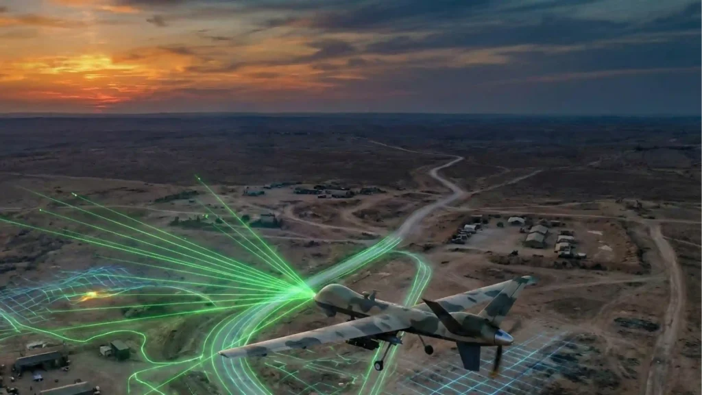 Aerial view of a desert defense test range at sunset with an unmanned aircraft and green and blue target-illumination paths across the ground.