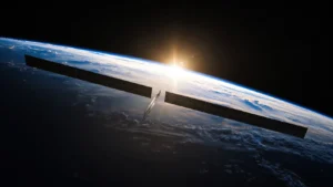 Communications satellite with long solar arrays above Earth at sunrise.